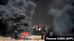 Një palestinez mban flamurin kombëtar, teksa tymi mbulon qiellin, gjatë përleshjeve mes palestinezëve dhe forcave izraelite në kufirin Gaza-Izrael. 14 maj, 2018