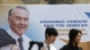 Men walk past an election poster of Kazakh President Nursultan Nazarbaev in Almaty.