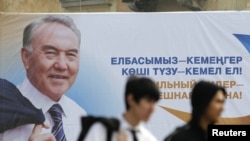 Men walk past an election poster of Kazakh President Nursultan Nazarbaev in Almaty.