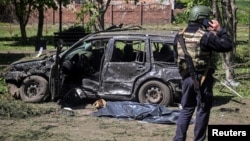 A police officer stands near a destroyed car and covered victim at the site of a Russian missile strike in the village of Zolochiv, Kharkiv region, Ukraine, on May 1.
