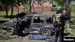 Policajac stoji u blizini uništenog automobila i pokrivene žrtve na mjestu ruskog raketnog napada u selu Zoločiv, oblast Harkiv, Ukrajina, 1. maja 2024.