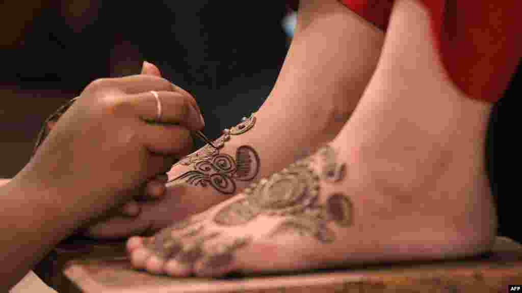 Pakistani beauticians apply traditional henna designs to the hands and feet of customers ahead of Eid al-Fitr in Karachi