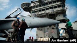 A pilot speaks to a crew member by an F/A-18 fighter jet on the deck of the USS Abraham Lincoln aircraft carrier in the Arabian Sea, June 3, 2019