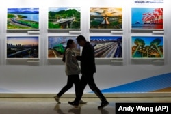 People walk by a display board showcasing China's construction projects at the media center of the Belt and Road Forum in Beijing.