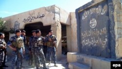 Iraqi policemen stand in front of a a flag belonging to the Islamic State (IS) group painted on a wall in a town outside Tikrit on March 8, where Iraqi continue their assault. 