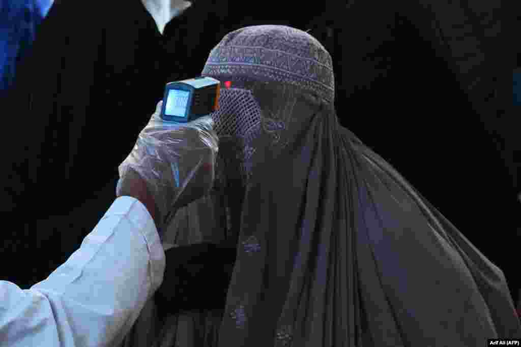 A health official checks the body temperature of a burqa-clad woman passenger amid concerns over the spread of the coronavirus at the railway station in Lahore, Pakistan, on March 19. (AFP/Arif Ali)