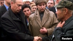 Russian President Vladimir Putin (left) shakes hands with an unidentified relative of a crew member of the Kursk, as Irina Lyachin (center), the wife of the commander of the submarine, looks on, in the town of Vidyayevo on August 22, 2000.