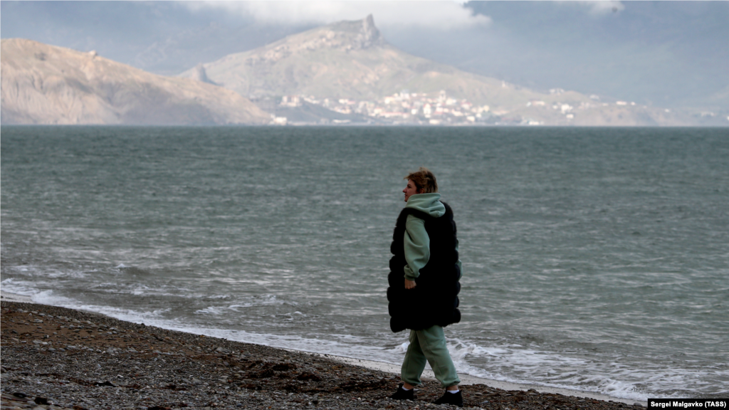 Краєвид на гірський масив Карадаг і самотня відпочивальниця на узбережжі Чорного моря