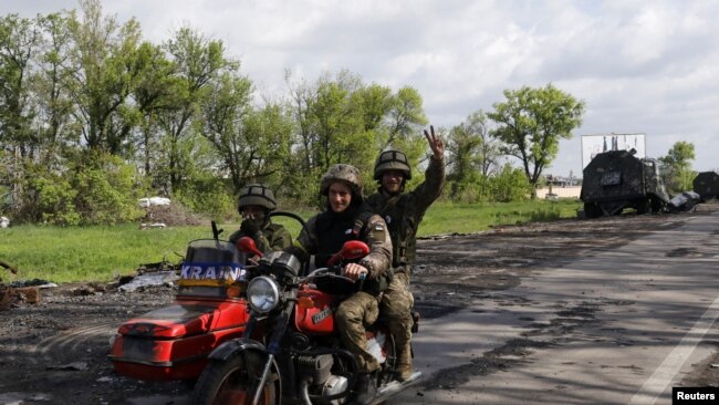 Ukrainian servicemen ride a motorcycle on a road outside a village recently retaken by Ukrainian forces near Kharkiv on May 13. 