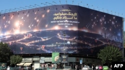 Pankarta në sheshin Enqelab, fotografuar në tetor 2024, që paraqet një shi raketash që godasin Izraelin. Teksti përfshin një frazë në farsi: “Nëse doni luftë, ne jemi mjeshtrit e luftës”.