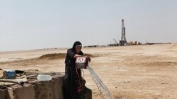 Gheyzaniyeh -- A local woman takes water from a well while in the background an oil well is visible.