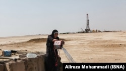 Gheyzaniyeh -- A local woman takes water from a well while in the background an oil well is visible.