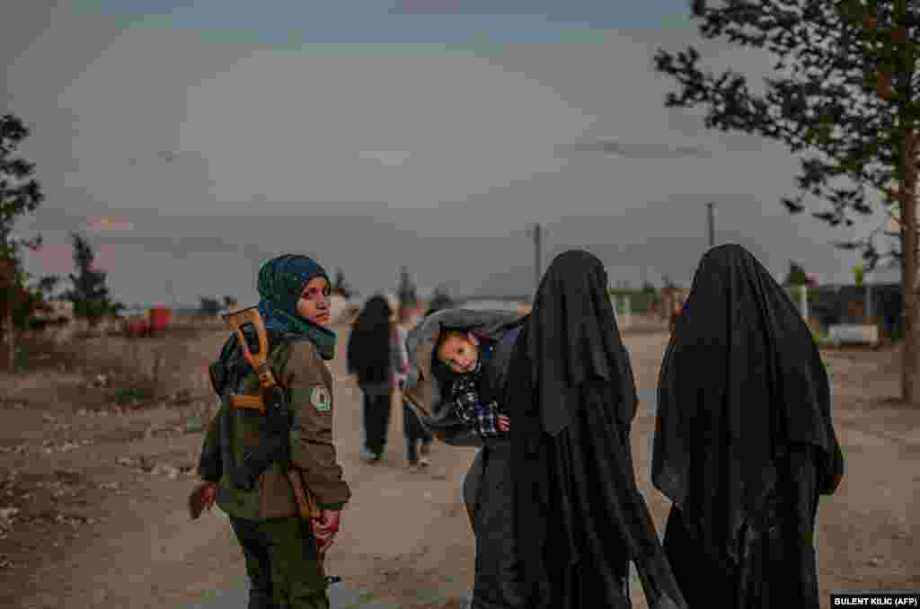 Veiled women, reportedly members of Islamic State and wives of the extremists, walk under the supervision of a female fighter from Kurdish-led Syrian Democratic Forces (SDF) in northeastern Syria. (AFP/Bulent Kilic)