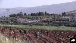 The Israeli village of Metulla, background, is seen from the Lebanese-Israeli border as Syrian farmers work in the village of Kfar Kila, in southeast Lebanon, Wednesday, May 20, 2020. Twenty years after Hezbollah guerrillas pushed Israel's last troops fro