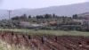 The Israeli village of Metulla, background, is seen from the Lebanese-Israeli border as Syrian farmers work in the village of Kfar Kila, in southeast Lebanon, Wednesday, May 20, 2020. Twenty years after Hezbollah guerrillas pushed Israel's last troops fro