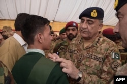 FILE: Pakistani army chief General Qamar Javed Bajwa (R) gives his autograph to a student at the Army Public School, on the second anniversary of an attack on the school. in Peshawar in December 2016.