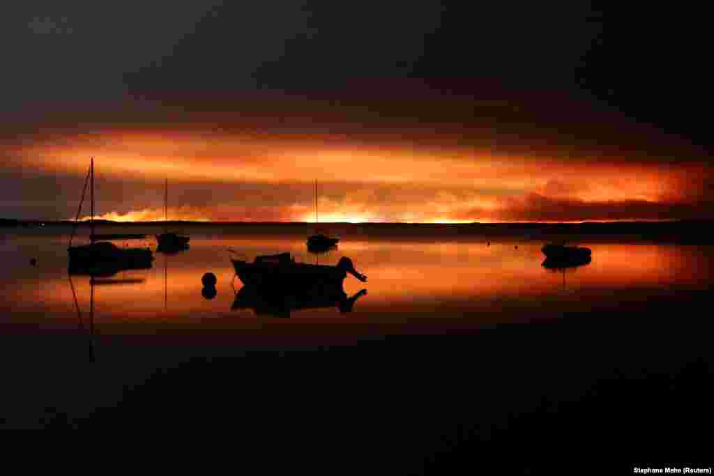 Varka të ankoruara në Lakano të Francës, teksa zjarret digjen në një zonë pyjore aty pranë. 