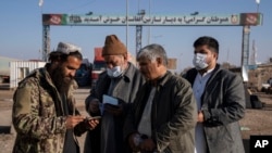 A Taliban fighter checks the passports of Afghans crossing into Iran at the border crossing of Islam Qala in the western Afghan province of Herat.