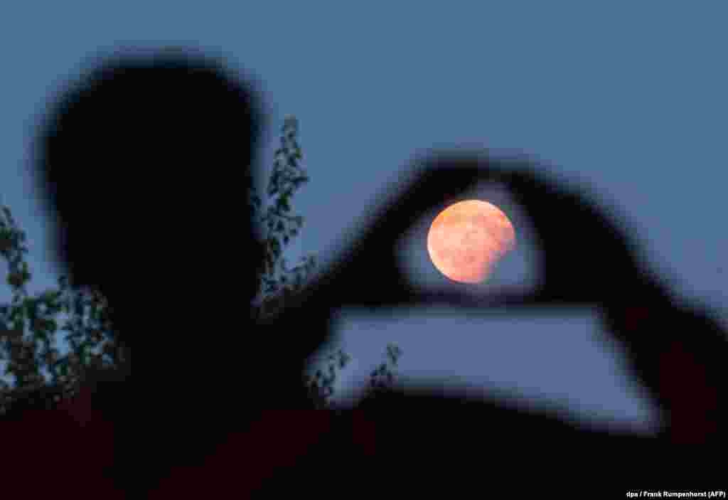 Një njeri bën sikur mban me duar hënën, në një eklips të pjesshëm të saj në Frankfurt, Gjermani, më 7 gusht.&nbsp;