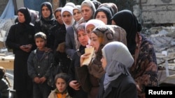 People wait to collect food aid distributed by United Nations Relief and Works Agency at the Yarmouk refugee camp. The camp has been suffering from extreme food shortages in recent months, which has left many malnourished or even starving. 