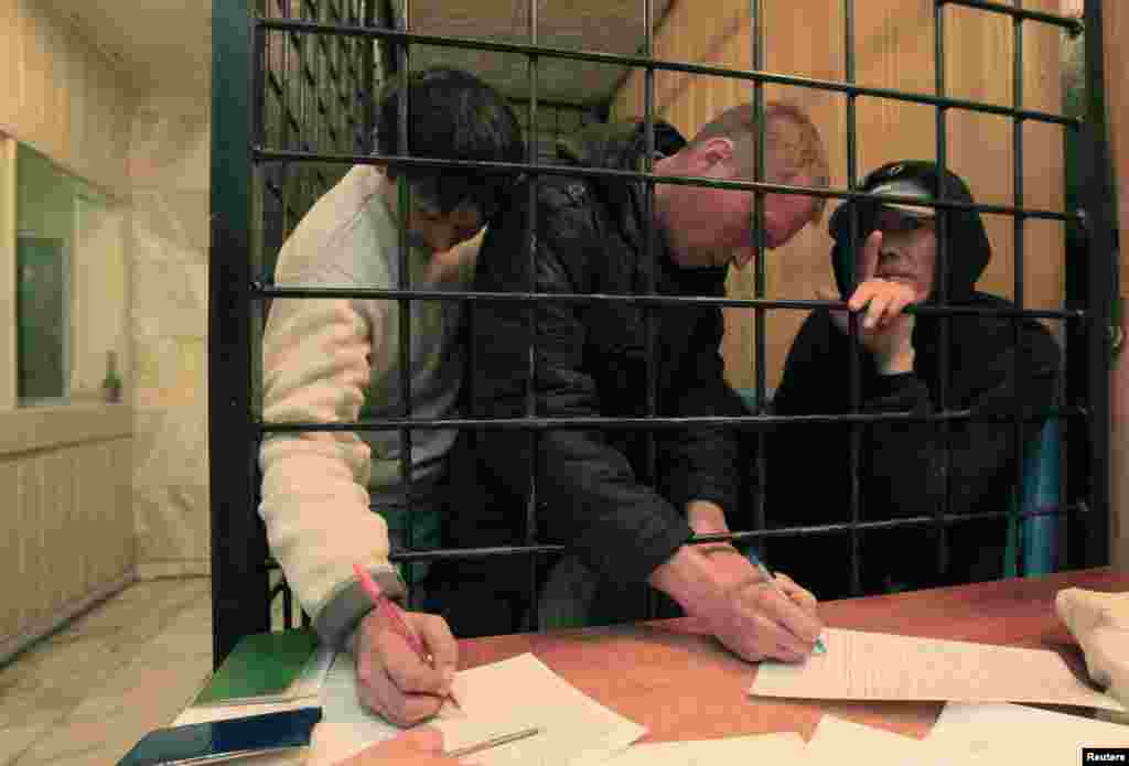 Detained migrants fill out paperwork in a holding cell.