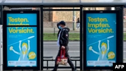 Një burrë shihet duke ecur në Berlin, para mbishkrieve që tregojnë për rreziqet e pandemisë dhe bëjnë thirrje për vaksinim.