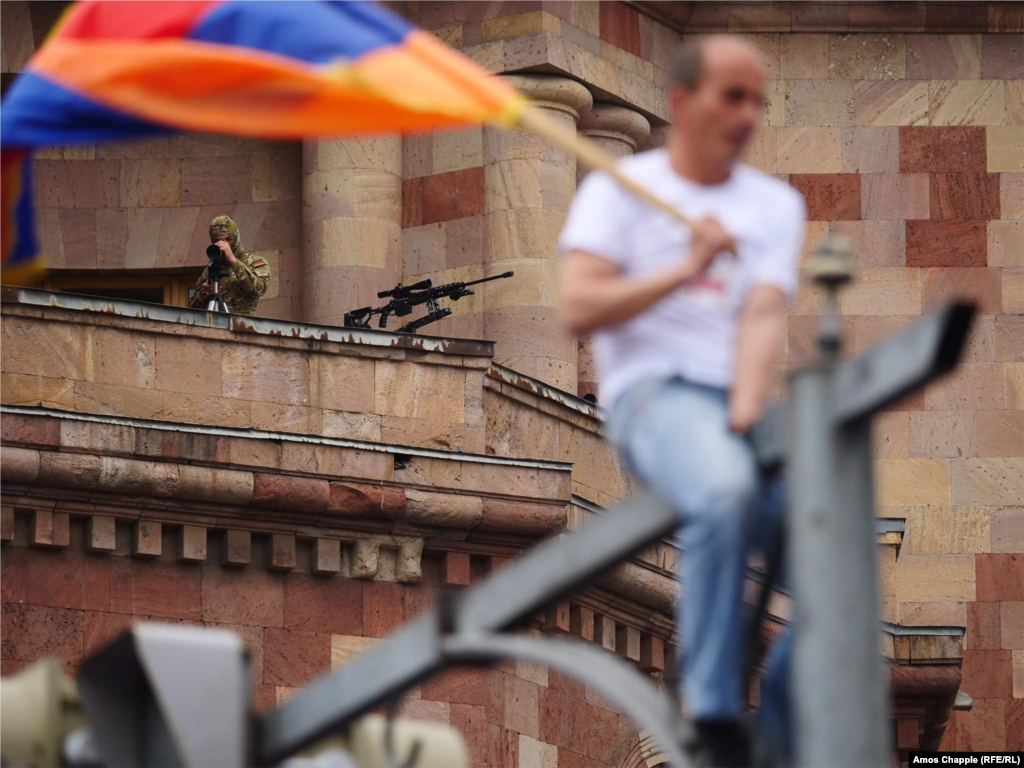 Masked snipers with rifles keep watch from a government building overlooking Republic Square in Yerevan, Armenia, on May 8, as people celebrate the election of opposition leader Nikol Pashinian.&nbsp;RFE/RL photographer Amos Chapple recalls how he photographed the street protests that toppled Prime Minister Serzh Sarkisian and his government in an interactive story,&nbsp;Caught Up In A Revolution. (Amos Chapple, RFE/RL)