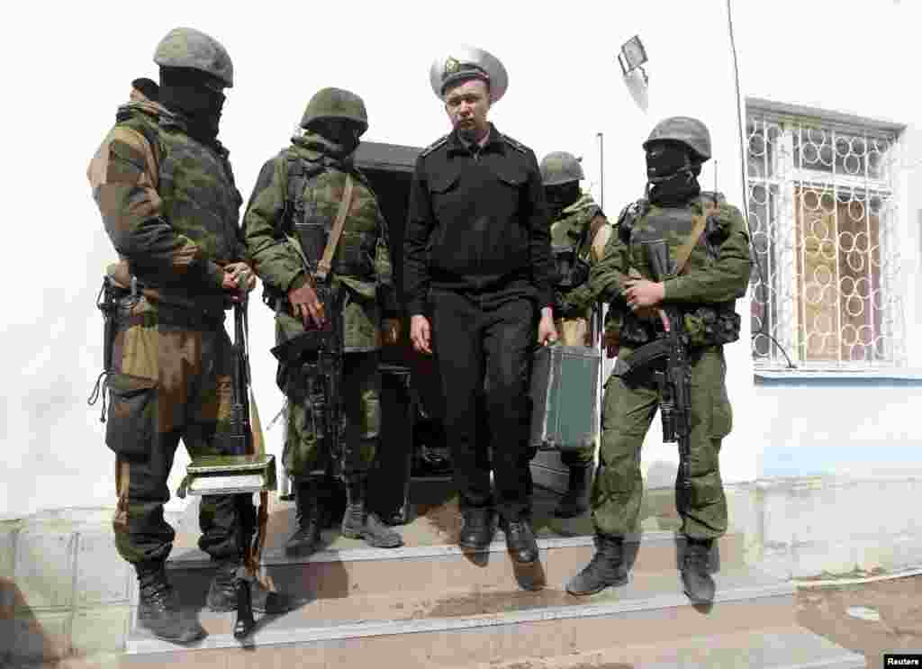 Украінскі марскі афіцэр праходзіць паміж узброенымі людзьмі, пакідаючы штаб-кватэру ваенна-марскіх сіл у Севастопалі