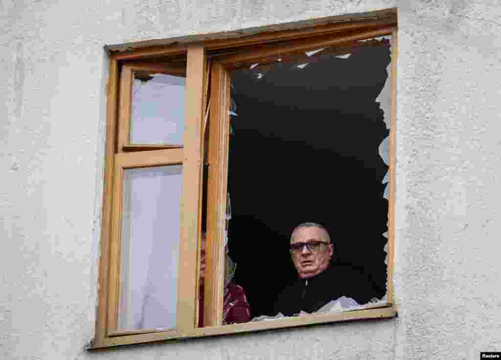 Местные жители смотрят из разбитого окна на место удара российского беспилотника, Харьков, Украина, 25 марта 2026 года. REUTERS/Sofiia Gatilova