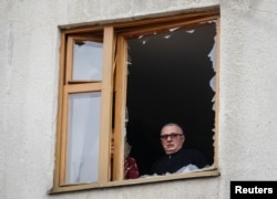 A resident of Kharkiv looks out of a window broken by a Russian drone strike in March.