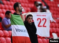 Fanii iranieni țin un steag al Iranului pe care scrie „Femei Viață Libertate” și o replică de tricou în memoria lui Mahsa Amini, înainte de meciul Țara Galilor - Iran din 25 noiembrie 2022, de la Cupa Mondială de fotbal din Qatar.