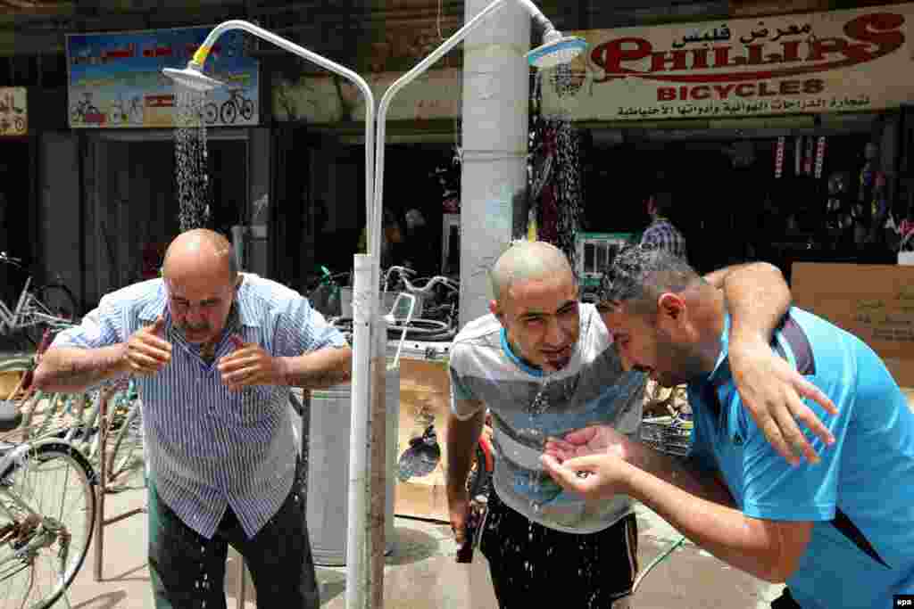 Iraqi men cool themselves under a public shower at a street in central Baghdad. Media reported that the temperature rose to more than 50 degrees Celsius in Baghdad and southern Iraq, which led to the Iraqi government announcing a two-day public holiday due to the heatwave. (epa/Ali Abbas)