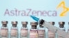 Vials labeled "AstraZeneca COVID-19 Coronavirus Vaccine" and a syringe are seen in front of a displayed AstraZeneca logo, March 10, 2021.