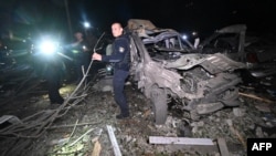 A Ukrainian police officer stands next to a destroyed car following a Russian missile attack in Kharkiv late on September 21. At least 12 people were injured.