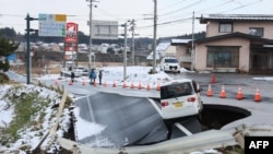د جاپان په توهوکو ښار کې تر زلزلې وروسته د سړک یوه برخه ړنګه شوې او یو ګاډی بند پاتې دی - د ډېسېمبر نهمې انځور.