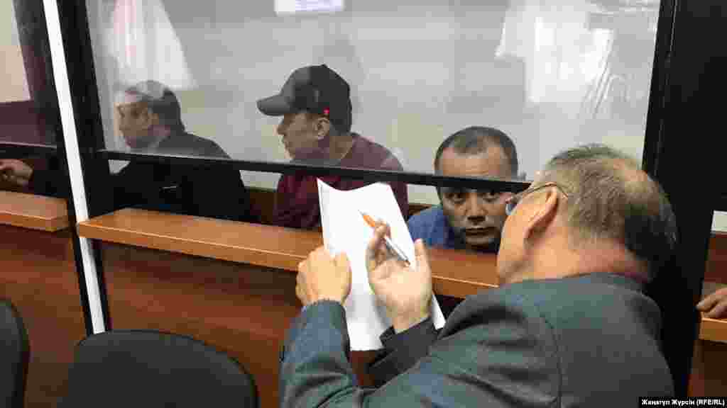 Өртенген автобус ісі бойынша күдікті деп танылған жүргізушілер (әйнек камера ішінде солдан оңға қарай) - Барат Таңатов, Нұржан Қырғызбаев, Мақсат Пернебеков сотта адвокат Хайрулла Әлимағамбетовпен сөйлесіп отыр. Айыпталушылар бес жылға сотталды. Ақтөбе. 3 қыркүйек 2018 жыл. 