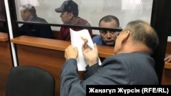 Өртенген автобус ісі бойынша күдікті деп танылған жүргізушілер (әйнек камера ішінде солдан оңға қарай) Барат Таңатов, Нұржан Қырғызбаев, Мақсат Пернебеков және адвокат Хайрулла Әлимағамбетов. Ақтөбе, 3 қыркүйек 2018 жыл.