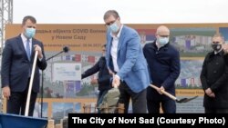 Aleksandar Vučić (drugi s leva) polaže kamen temeljac za novu COVID-19 bolnicu u Novom Sadu. Desno od njega je predsednik Vlade Vojvodine Igor Mirović, a levo, takođe sa lopatom u ruci, gradonačelnik Novog Sada Miloš Vučević. Nebojša Stefanović (na slici krajnje desno), bivši šef policije, a danas ministar odbrane, posmatra događaj dan uoči najavljenog njegovog saslušanja u policiji zakazanog za 29. april 2021.
