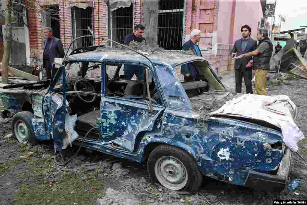 People stand next to a destroyed car in a damaged area of the city of Ganca following a reported Armenian rocket strike on October 4. (TASS/Valery Sharifulin)