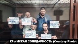 Фігуранти другої сімферопольської справи «Хізб ут-Тахрір» із плакатами. Перший праворуч у другому ряду Ремзі Бекіров, травень 2021 року