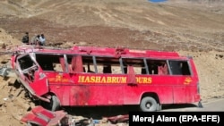 FILE: People stand beside the wreckage of a passenger bus at the scene of its accident near Chilas in Gilgit-Baltistan in September 2019.