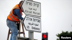 Рабочий устанавливает дорожный знак "Посольство США" на улице в Иерусалиме 