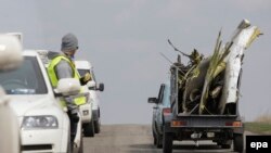 Участник следственной группы смотрит на автомобиль, в котором перевозят обломок самолета в Донецкой области, 16 апреля 2015