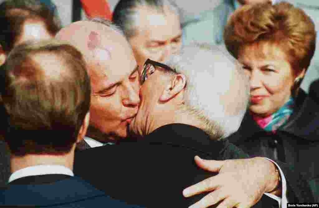 Președintele sovietic Mihail Gorbaciov (stânga) îl îmbrățișează pe Erich Honecker,&nbsp;liderul Republici Democrate Germane și al Partidului Comunist al germanei de Est, la sosirea lui Gorbaciov pe aeroportul Schoenefeld din Berlinul de Est, 6 octombrie 1989. Cei doi au recreat sărutul lui&nbsp;Honecker cu Brejnev, din 1979.