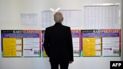 Fotografija: Glasač ispred plakata na jezicima konstitutivnih naroda BiH, srpskom, hrvatskom i bosanskom, uoči parlamentarnih izbora 2018. godine.