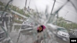 An ethnic Uyghur woman is seen through the broken window of a car dealership as cars damaged during the July unrest are visible in the background in a mainly Uyghur neighborhood in Urumqi.