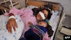 Afghan woman Reza Gul, 20, whose nose was sliced off by her husband in an attack, lies on a bed with her baby as she receives treatment at a hospital in the northern province of Faryab on January 19.