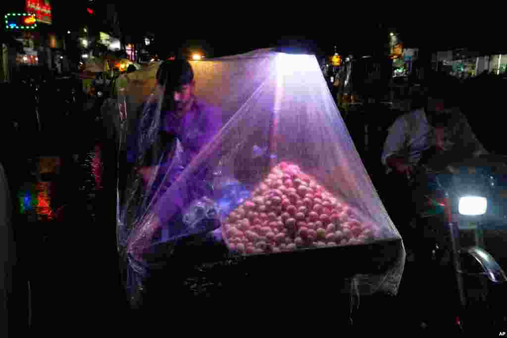 A roadside vendor waits for a customer with a plastic sheet over him to protect himself from the rains in Lahore, Pakistan.