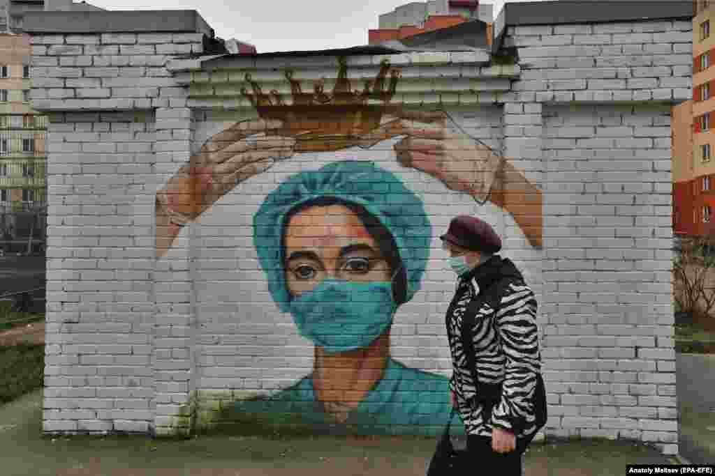 Žena prolazi pored grafita na temu korona virusa koji prikazuju medicinara u mestu Bugri, izvan ruskog grada Sankt Peterburga. (epa-EFE / Anatolij Maltsev)