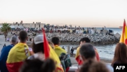 Manifestanții care se opun prezenței migranților privesc grupul de migranți care și-au instalat tabăra pe plaja Trampolin din Ceuta, pe 28 august 2026.